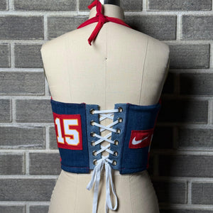 Back view of a Kansas City Chiefs women’s halter corset top featuring denim panels, white lace-up closure, red tie neck, and number 15 with Nike logo patches.
